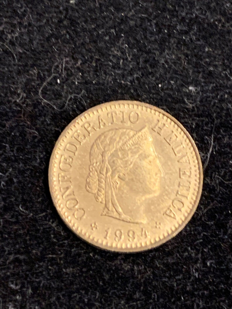 Puede incluir: Una moneda de color dorado con la inscripci&oacute;n "CONFEDERATIO HELVETICA" y el a&ntilde;o "1994" alrededor del borde.