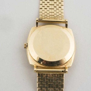 May include: A gold-tone wristwatch with a square face and a gold-tone metal band. The watch has a plain back.