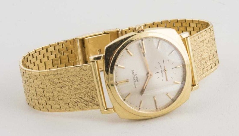 May include: A gold Patek Philippe Geneve wristwatch with a square face and a gold metal band.