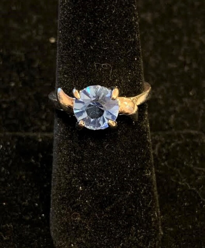 Pu&ograve; includere: Un anello d'argento con una pietra preziosa blu chiaro. L'anello ha una fascia attorcigliata.