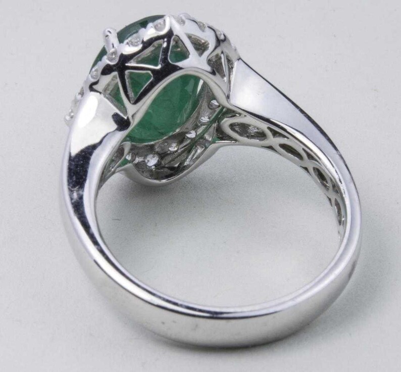 Puede incluir: Un anillo de plata con una gran piedra preciosa verde rodeada de piedras preciosas blancas m&aacute;s peque&ntilde;as.