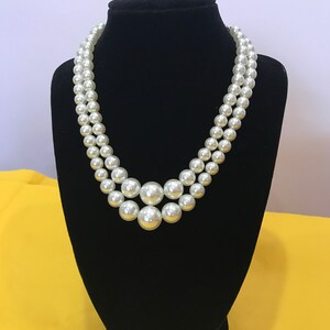 May include: A double strand pearl necklace with large, white pearls. The necklace is displayed on a black velvet stand.