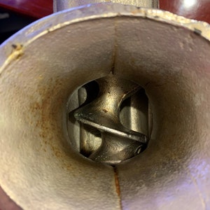 May include: Close-up of a vintage metal meat grinder. The interior shows the auger and the inside of the grinder. The metal has a worn, aged appearance with some rust. The grinder is designed for food preparation.