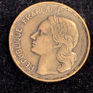 Puede incluir: Una moneda de bronce con las palabras "REPUBLIQUE FRANCAISE" alrededor del borde. La moneda presenta un perfil de una mujer con el pelo recogido hacia atr&aacute;s. La moneda tambi&eacute;n tiene la inscripci&oacute;n "GGUILLRAUD".