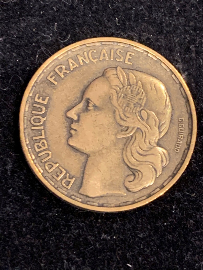 Puede incluir: Una moneda de bronce con las palabras "REPUBLIQUE FRANCAISE" alrededor del borde. La moneda presenta un perfil de una mujer con el pelo recogido hacia atr&aacute;s. La moneda tambi&eacute;n tiene la inscripci&oacute;n "GGUILLRAUD".