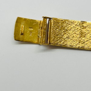 May include: Close-up of a gold watch band with a clasp. The clasp is open and shows the inscription "14K" inside.
