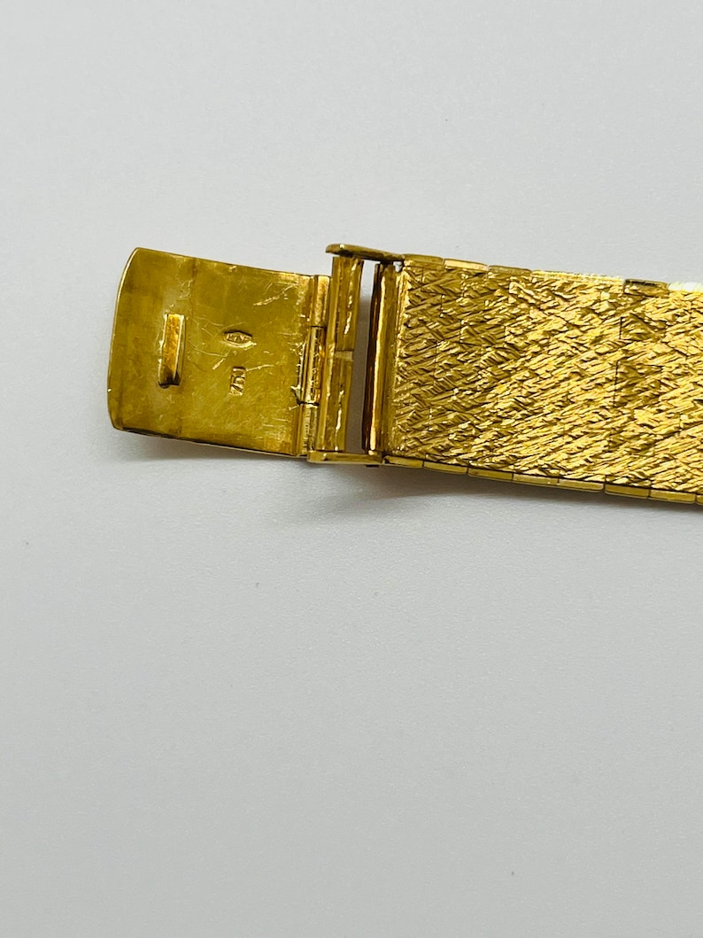 May include: Close-up of a gold watch band with a clasp. The clasp is open and shows the inscription "14K" inside.