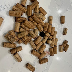 May include: A collection of used wine corks, some with the name of the winery printed on them. The corks are various shades of brown and beige.