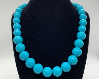 May include: A turquoise blue beaded necklace with large round beads. The necklace is displayed on a black velvet bust form.