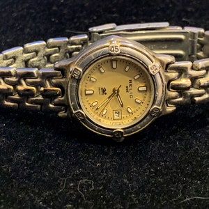 Peut inclure: Une montre-bracelet argent&eacute;e avec un bracelet dor&eacute;. Le cadran de la montre est de couleur cr&egrave;me avec des aiguilles noires et des chiffres romains noirs. Le cadran de la montre a &eacute;galement une fen&ecirc;tre de date &agrave; 3 heures. La montre est &eacute;tiquet&eacute;e "RELIC 100m".