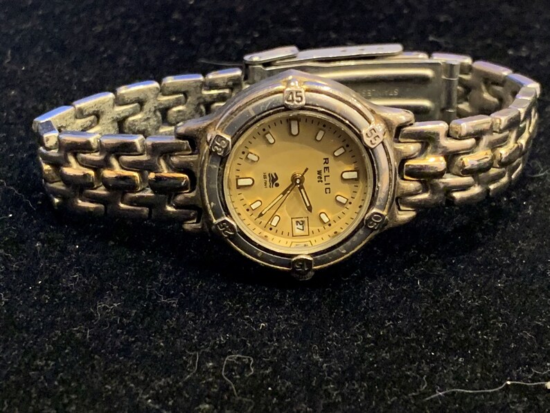 Peut inclure: Une montre-bracelet argent&eacute;e avec un bracelet dor&eacute;. Le cadran de la montre est de couleur cr&egrave;me avec des aiguilles noires et des chiffres romains noirs. Le cadran de la montre a &eacute;galement une fen&ecirc;tre de date &agrave; 3 heures. La montre est &eacute;tiquet&eacute;e "RELIC 100m".