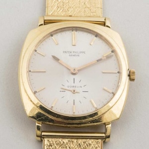 May include: A gold Patek Philippe Geneve wristwatch with a white face and gold hands. The watch has a square face and a gold band. The watch face has the text "Patek Philippe Geneve" and "Gubelin" printed on it.