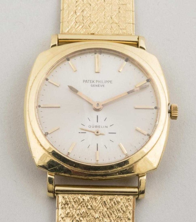 May include: A gold Patek Philippe Geneve wristwatch with a white face and gold hands. The watch has a square face and a gold band. The watch face has the text "Patek Philippe Geneve" and "Gubelin" printed on it.