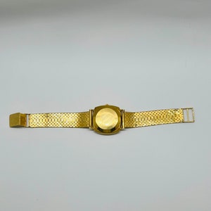 May include: A gold-tone wristwatch with a square face and a gold-tone metal band.
