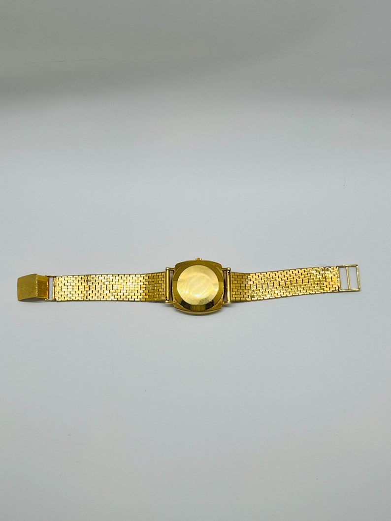May include: A gold-tone wristwatch with a square face and a gold-tone metal band.