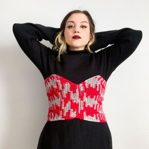 Puede incluir: Una mujer con una camisa negra de cuello alto y un top de ganchillo rojo y blanco. El top tiene un patrón geométrico.