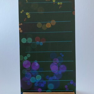 May include: A black card with the word "Affirmations" written in blue cursive on a background of colorful bokeh lights. The card is standing on a wooden stand.