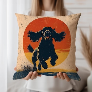 Può includere: Cuscino quadrato con una silhouette di cane nero che salta davanti a un design retrò del tramonto. Il cuscino ha un aspetto vintage invecchiato con uno sfondo color crema e un bordo blu navy e giallo.