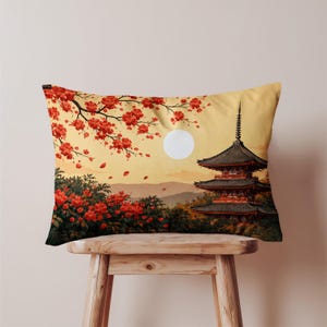 Könnte beinhalten: Rechteckiges Zierkissen mit einer japanischen Landschaftsszene. Das Design umfasst eine Pagode, rote Blütenzweige und einen Vollmond vor gelbem Hintergrund. Das Kissen liegt auf einem Holzschemel.