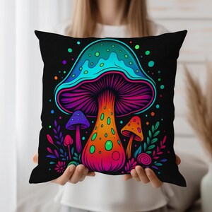 Op de afbeelding: Zwart vierkant kussen met een levendige illustratie van kleurrijke paddenstoelen. De centrale paddenstoel heeft een turquoise kap, een oranje steel en paarse kieuwen. Kleinere paddenstoelen in paars en oranje zijn ook afgebeeld, omringd door kleurrijke stippen en bladeren.
