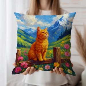 Puede incluir: Cojín cuadrado con un gato atigrado naranja posado en una valla de madera, con un fondo de montañas, campos verdes y flores. El cojín tiene un fondo de cielo azul.