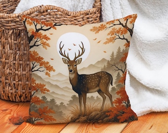 May include: Square decorative pillow featuring a deer in a forest scene. The artwork depicts a deer with large antlers standing in front of a full moon, surrounded by trees with orange leaves. The background shows mountains and a forest.