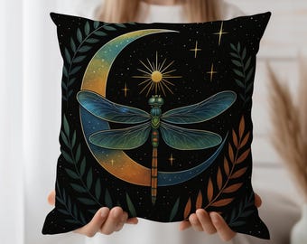 Puede incluir: Cojín decorativo cuadrado con un diseño celestial. El cojín negro presenta una luna creciente en tonos azules y naranjas, un sol, estrellas y una libélula. Ramas frondosas verdes y marrones enmarcan el diseño.
