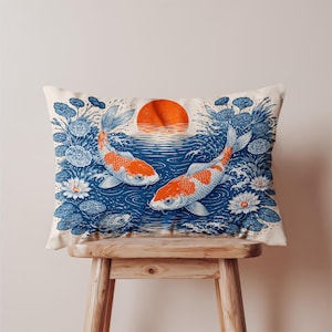 May include: Rectangular pillow featuring a Japanese-inspired design. Two orange and white koi fish swim in blue water with a setting orange sun in the background. The pillow is decorated with blue water lilies and white flowers.