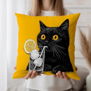 Può includere: Cuscino giallo quadrato con un gatto nero con occhi gialli, raffigurato con un cocktail. Il gatto beve da un bicchiere con cubetti di ghiaccio e una fetta di limone. Il cuscino è quadrato.