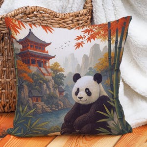 Könnte beinhalten: Dekoratives Kissen mit einem Panda in einer asiatischen Landschaft. Das Design zeigt eine traditionelle Pagode, Bambus und Herbstlaub in Rot-, Orange- und Grüntönen. Der Panda ist schwarz und weiß.