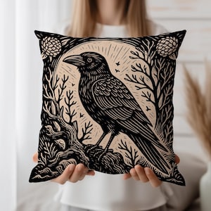 May include: Black and beige decorative pillow featuring a detailed illustration of a raven perched on a branch, surrounded by stylized trees and floral elements. The design has a vintage, woodcut style.