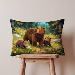 May include: Rectangular pillow featuring a vibrant illustration of a bear family in a forest setting. The image shows a large brown bear with two cubs amidst wildflowers and tall green trees. The pillow is placed on a wooden stool.