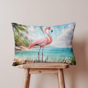 May include: A rectangular cushion with a pink flamingo standing in shallow turquoise water. The background depicts a tropical beach scene with palm trees, blue sky, and white clouds. The cushion is placed on a wooden stool.