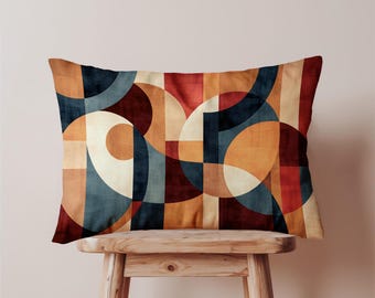 Könnte beinhalten: Rechteckiges Zierkissen mit geometrischem Muster. Das Design zeigt überlappende Formen in Blau-, Orange-, Rot- und Cremetönen. Das Kissen liegt auf einem kleinen Holzschemel und präsentiert sein Design und seine Textur.