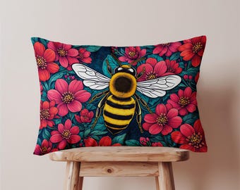 May include: Rectangular decorative pillow featuring a large bee with yellow and black stripes, white wings, and a black head. The bee is centered on a dark blue background with red flowers and green leaves. The pillow is placed on a wooden stool.