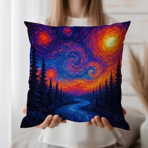 Puede incluir: Cojín cuadrado con una pintura impresionista vibrante de un cielo estrellado sobre un bosque y un río. La obra de arte presenta remolinos de azules, naranjas y morados. El cojín está sostenido por una persona. Aproximadamente 40 cm x 40 cm.