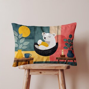 May include: Decorative rectangular pillow featuring a whimsical illustration of a white bear relaxing in a hanging chair. The design includes a yellow moon, plants in vases, and a candle, set against a colorful geometric background.