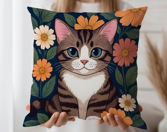 以下が含まれることがあります： 青い目、茶色の縞模様、白い胸を持つ漫画の猫が描かれた正方形の装飾枕。 猫は、オレンジ色、桃色、白色の花と、濃い青色の背景に緑色の葉で囲まれています。