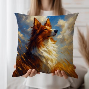 Puede incluir: Cojín cuadrado decorativo con una imagen pintada de un perro con pelaje marrón y blanco, sobre un fondo de cielo azul con nubes y trigo dorado. El cojín es sostenido por una persona.