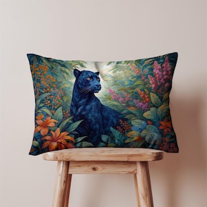 Peut inclure: Coussin rectangulaire représentant une panthère noire dans une jungle luxuriante. La panthère a des yeux orange et est entourée de fleurs et de feuillages colorés dans des tons de vert, orange et rose. Le coussin est posé sur un tabouret en bois.