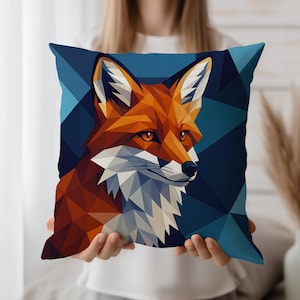 Puede incluir: Un cojín cuadrado decorativo con un diseño geométrico de la cabeza de un zorro. El zorro está representado en tonos naranja, marrón y blanco sobre un fondo geométrico azul oscuro. Un accesorio de decoración para el hogar.