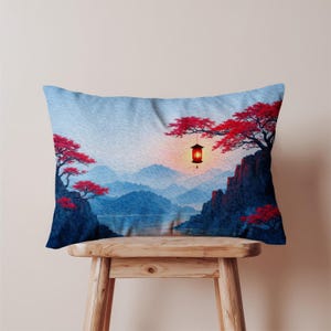 May include: Rectangular pillow featuring a serene landscape with blue mountains, a lake, and red-leafed trees. A hanging lantern illuminates the scene. The pillow is placed on a wooden stool.