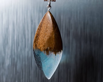 May include: A teardrop-shaped pendant necklace with a brown wood top and a clear blue resin bottom. The necklace is made with a blue leather cord.