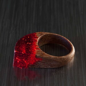 以下が含まれることがあります： 木製のバンドが付いた赤いレジンリング。レジンはキラキラした仕上げです。