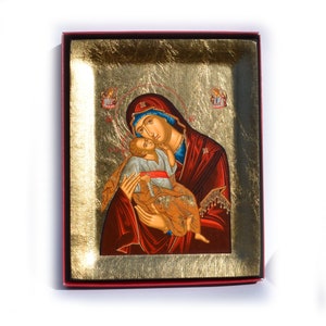 Puede incluir: Icono de la Virgen María y el Niño, presentado en una caja roja. El icono presenta un fondo dorado y una representación detallada de María con una túnica roja y un tocado azul, sosteniendo al niño. Se ven dos pequeñas figuras de ángeles.