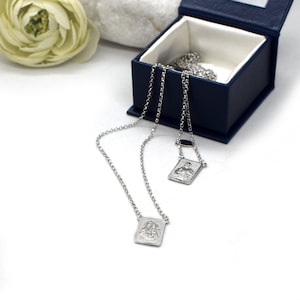 May include: Two silver necklaces with rectangular pendants featuring detailed engravings. The necklaces are displayed in a blue velvet box.