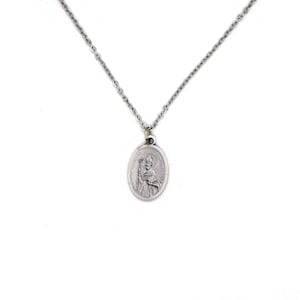 May include: Silver necklace with an oval pendant depicting a religious figure. The pendant hangs from a fine chain. The image is a close-up of the necklace against a white backdrop, emphasizing the pendant's detailed design and the chain's texture.