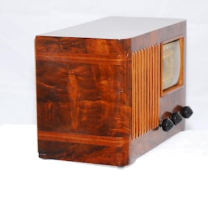 May include: A vintage wooden radio with a glossy, dark brown finish. The radio has a rectangular design, a speaker grill on the side, and three black knobs. It features a small, rectangular display.