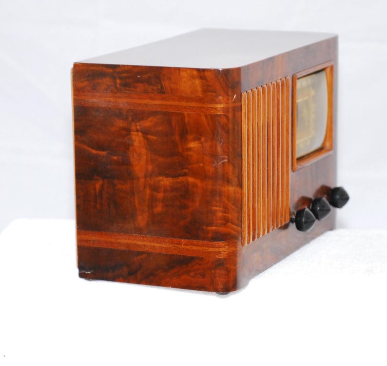 May include: A vintage wooden radio with a glossy, dark brown finish. The radio has a rectangular design, a speaker grill on the side, and three black knobs. It features a small, rectangular display.