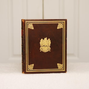 May include: A brown leather-bound book with gold accents and a gold crest on the front cover.